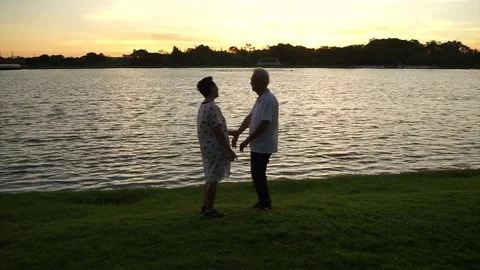 Asian senior couple exercise next to morning light with golden sunrise lake Stock Footage 70977648