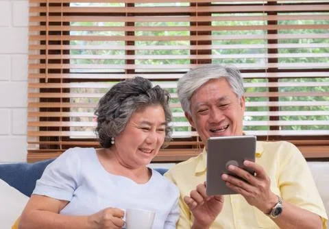 Asian senior couple using table compute and drink coffee sitting at sofa in l Stock Photos