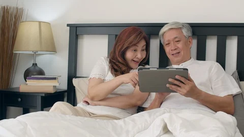 Asian senior couple using tablet on bed in bedroom at home in the morning. Stock Footage 114993974