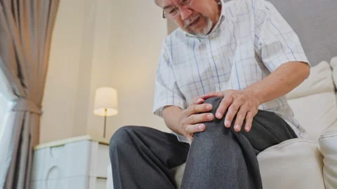 Asian senior elderly man sit on sofa, suffering from injured leg at home. Stock Footage 167844418
