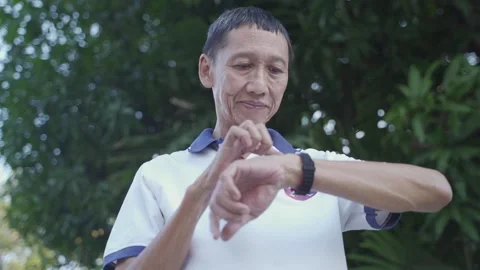 Asian senior elderly man touching smart watch activity tracker at park under tre Vídeos de archivo 157979645