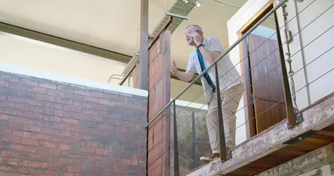 Asian senior man stepping onto loft checking phone, calling below pointing over Stock Footage 337026518