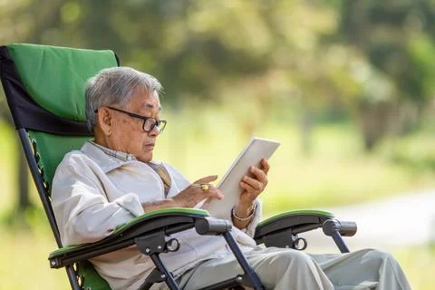Asian senior man using digital tablet on folding chairat natural park. The us Stock Photos