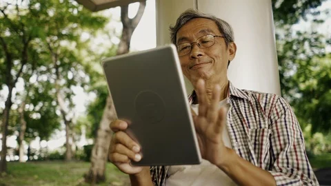 Asian senior man using tablet, sitting alone on the bench in the park Stock Footage 94643864