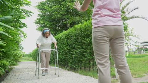 Asian senior mather walk with walker and adult daughter support in garden at Stock Footage 159297366