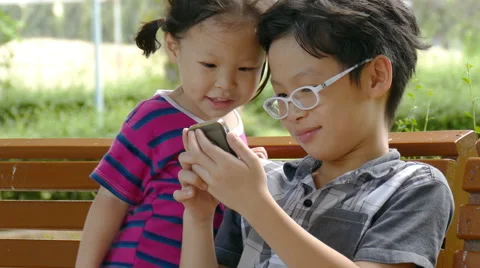 Asian siblings playing game on smart phone Stock Footage 64108952