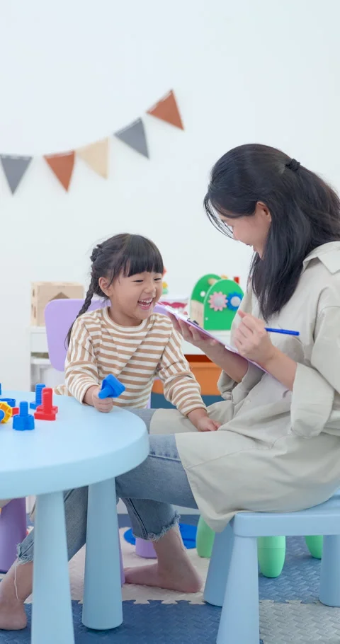 Asian single mother smiles while preschool daughter sits at play table and Stock Footage 339207094