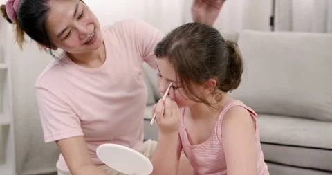 Asian single mother smiling while watching daughter apply eyeshadow with brush Stock Footage 307511433