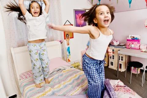 Asian sisters jumping on bed Stock Photos