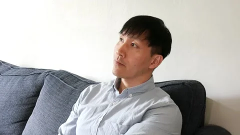 Asian sitting on a couch talking to someone and then getting up Stock-Footage 247480012