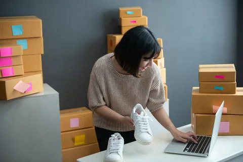 Asian smiling girl using smartphone to shoot white sneaker posted for sale on Stock Photos