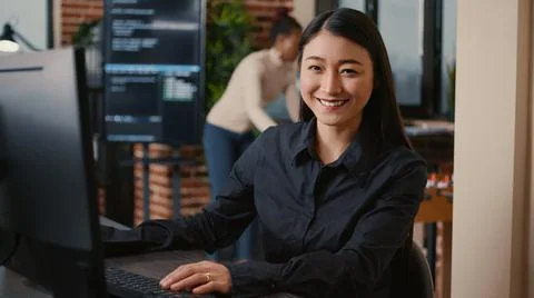 Asian software developer smiling and resuming work typing code on computer Foto stock