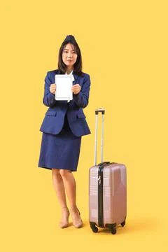 Asian stewardess with blank tablet computer and suitcase on yellow background Stock Photos
