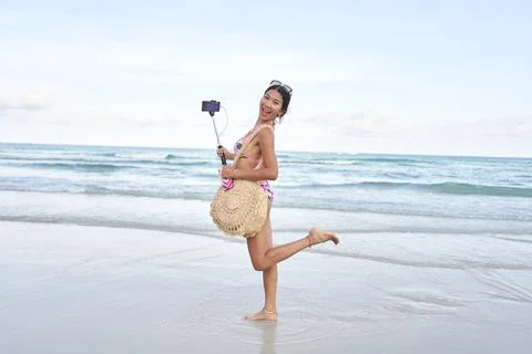 Asian streamer posing funny and holding a selfie stick with a mobile on a beach Stock Photos