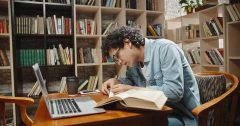 Asian student doing research in library using laptop in books, making a project 스톡 사진