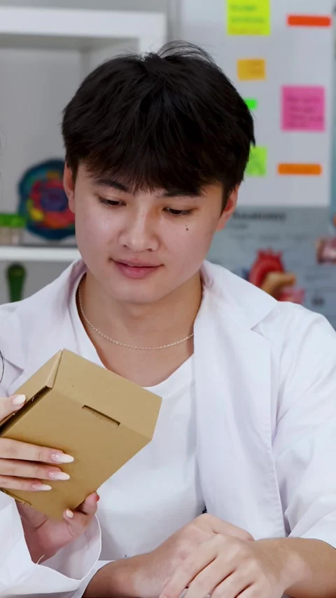 Asian Student in Lab Coat Examining Cardboard Box in Classroom Stock Footage 341662621