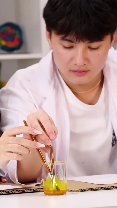 Asian Student in Lab Coat Mixing Yellow Liquid in Beaker Stock Footage 346447338