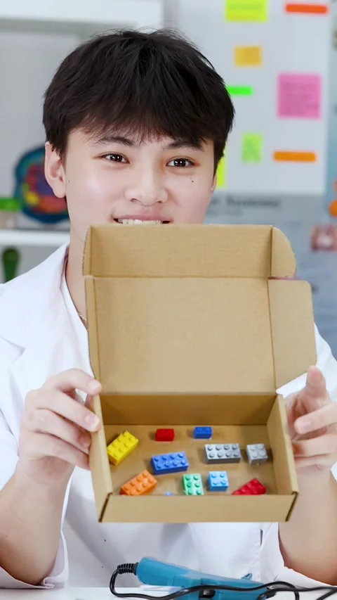 Asian Student in Lab Coat Showing Toy Bricks in Cardboard Box Stock Footage 341662773