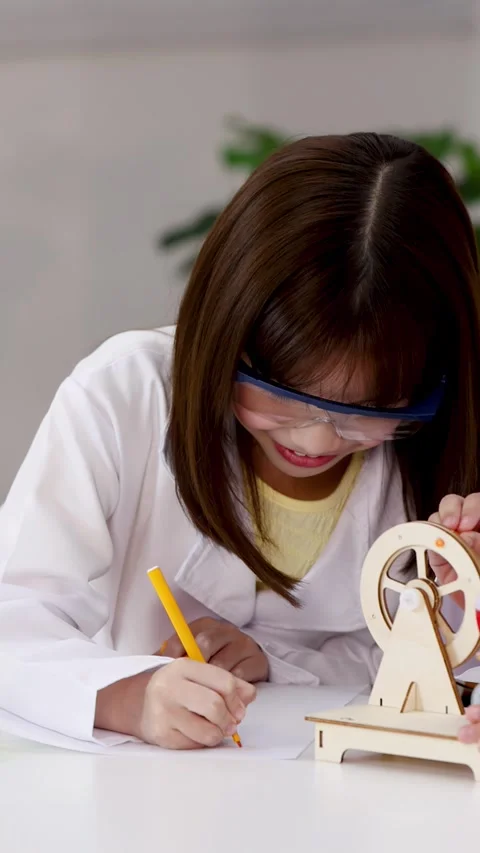 Asian Student in Lab Coat Writing Notes Near Wooden Science Model Stock Footage 339876965