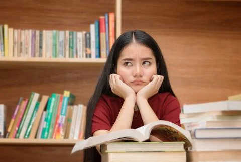 Asian student looking stressed while reading book preparing examination in li Stock Photos