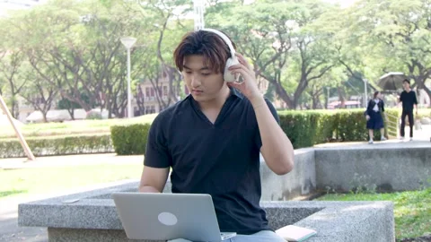Asian Student Putting on Headphones While Using Laptop at University Campus Stock Footage 334640983