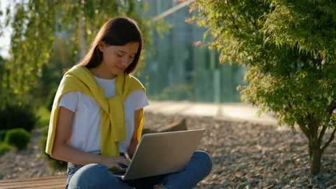 Asian student sitting on the bench studying on the laptop in the city centre Stock Footage 220604778