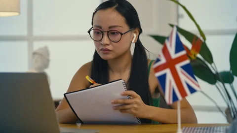 Asian student taking notes during virtual English course, focused on lesson Stock Footage 313720366