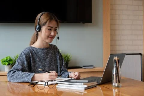Asian student taking notes in notebook and using laptop computer for e-learning Stock Photos