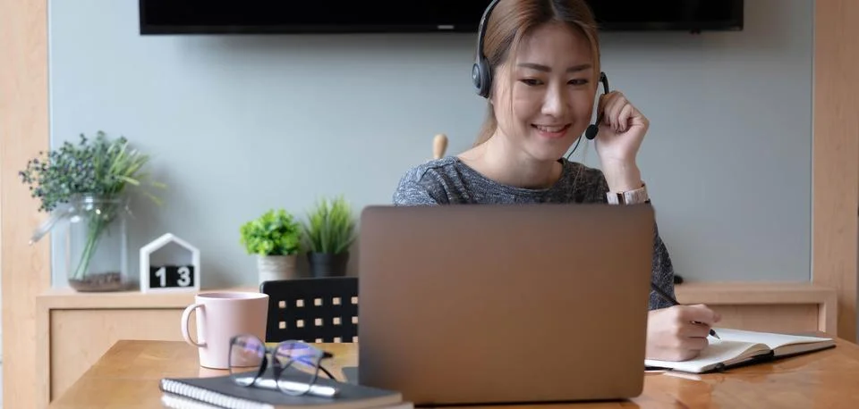 Asian student taking notes in notebook and using laptop computer for e-learning Stock Photos