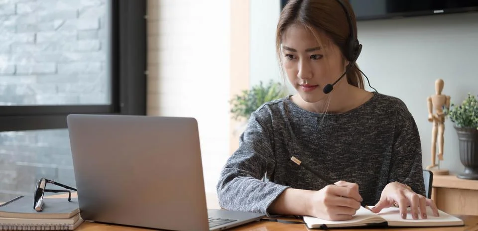 Asian student taking notes in notebook and using laptop computer for e-learning Stock Photos