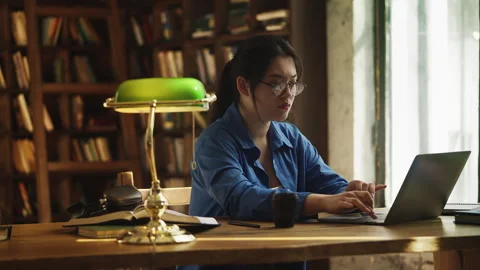 Asian student typing on laptop in a library, having problems with pc program 動画素材 331875393