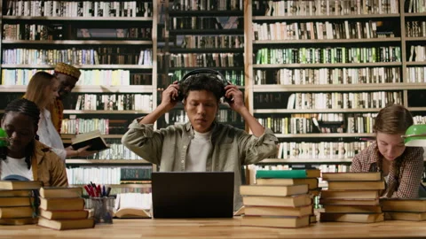 Asian student using headphones and taking notes with laptop and open book Stock Footage 337229899
