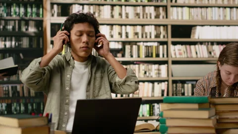 Asian student using headphones and taking notes with laptop and open book Stock Footage 337232709