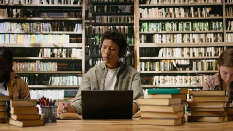 Asian student using headphones and taking notes with laptop and open book Stock Photos