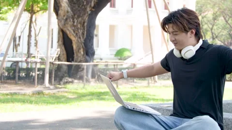 Asian Student Using Laptop and Headphones Outdoors on University Campus Stock Footage 334640991