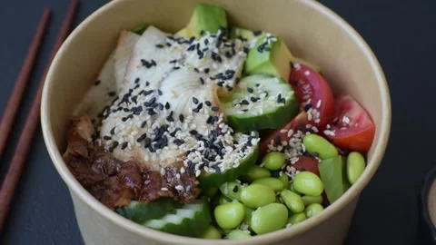 An Asian style bowl with eel, edamame, avocado, tomatoes, and lettuce. A eel and Stock Footage 345599652