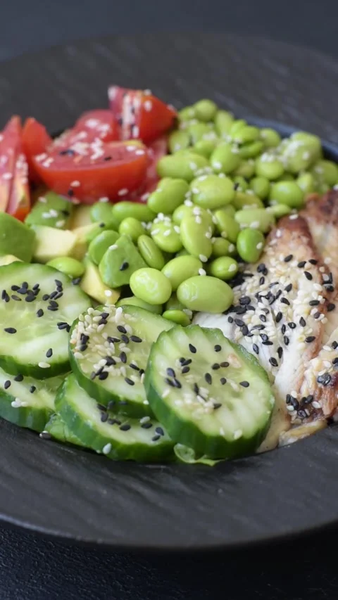An Asian style bowl with eel, edamame, avocado, tomatoes, and lettuce. A eel and Stock Footage 345599656