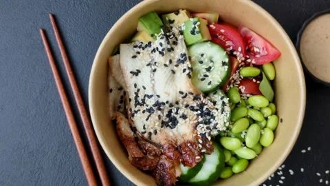 An Asian style bowl with eel, edamame, avocado, tomatoes, and lettuce. A eel and Stock Footage 345599751
