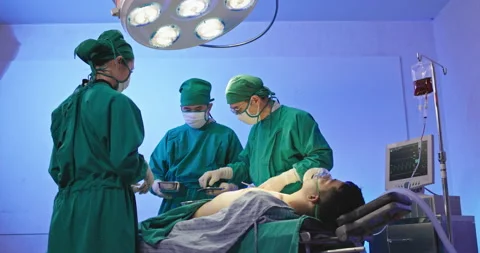 Asian team of surgeons is performing an operation on a patient in a hospital Stock Footage 230974801