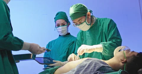 Asian team of surgeons is performing an operation on a patient in a hospital Stock Footage 230976764