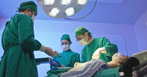 Asian team of surgeons is performing an operation on a patient in a hospital Stock Footage 230976804
