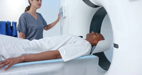 Asian tech wearing gray scrubs using panel, moving African American male into CT Stock Footage 336535832