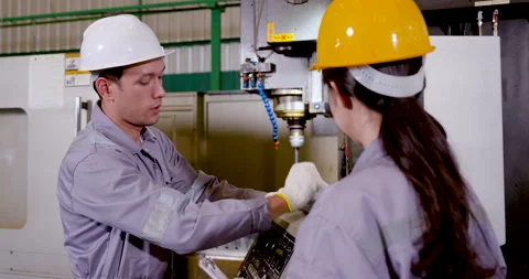 Asian technician points at CNC screen beside woman engineer, explaining program Stock Footage 338073768