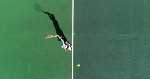 An Asian Tennis player serves filmed from above. Stock Footage