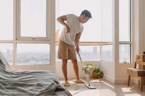 Asian Thai man using mop for cleaning floor in living room apartment, Man do Foto stock