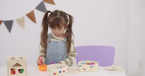 Asian toddler girl using plastic tongs and bowl to sort colorful toy pieces, Stock Footage 330169587