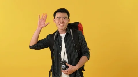 Asian tourist man with backpack clicks photo on camera and waves his hand Stock Footage 113909285