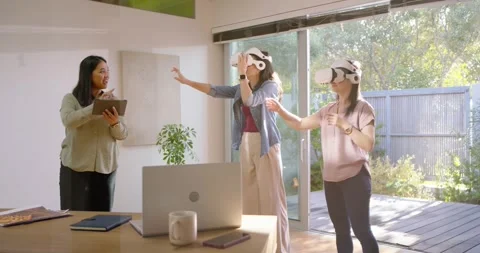 Asian trainer with tablet raising hand, speaking, training two women donning VR Stock Footage 335761475