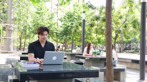 Asian University Student Using Laptop and Smartphone at Outdoor Campus Table Stock Footage 328786524