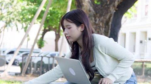 Asian University Student Using Laptop and Notebook in Sunny Campus Park Stock Footage 334165555